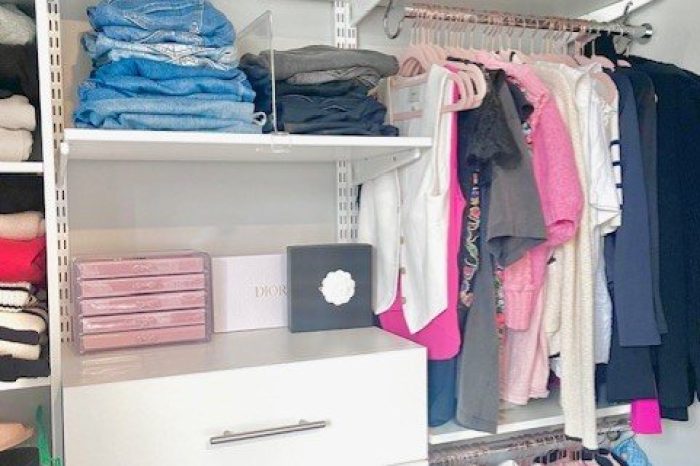 After picture of the newly designed and installed closet. There is a double hanging rod to the right side with a shelf above it. There is a tall 4 drawer dresser in the middle, the top of which has a pink jewelry box on it. As well as two shelves that hold jeans with shelf dividers in the space.